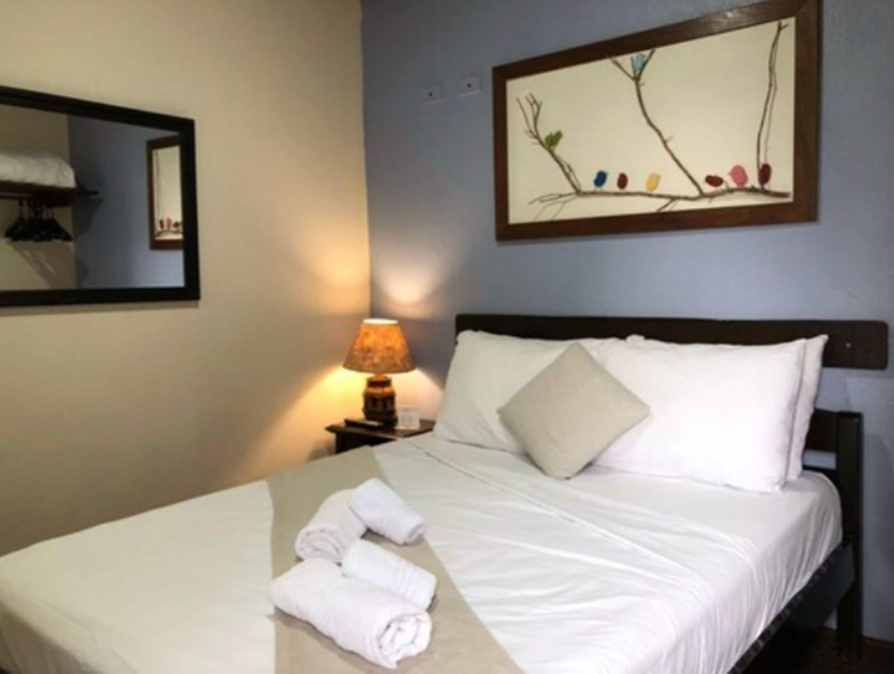 A neatly made bed with white linens, a lamp on a bedside table, and a framed artwork above the bed.