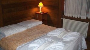 Ein Einzelbett mit weißer Bettwäsche und einer beigen Decke in einem Zimmer mit Holzwänden und einem weißen Heizkörper.