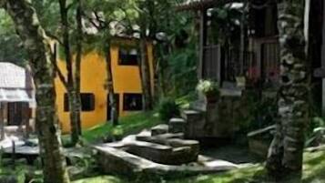 A rustic building with a sloped roof, surrounded by lush greenery and trees.