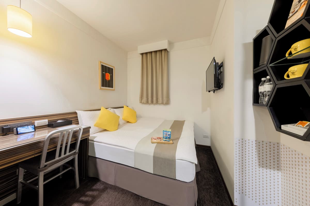 Habitación de hotel con cama, escritorio, silla y televisor en la pared.