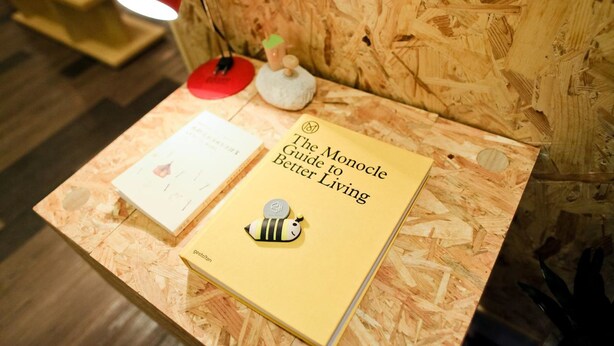 A book titled "The Monocle Guide to Better Living" on a wooden surface with a red lamp and a small decorative item in the background. - Bee House by Cosmos Creation-Taipei Main Station (Taipei)