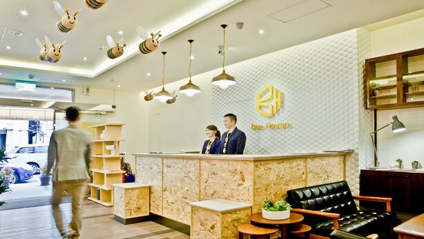 A reception area with a modern design, featuring a reception desk, a black leather sofa, and a wall with a honeycomb pattern. - Bee House by Cosmos Creation-Taipei Main Station (Taipei)