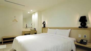 Quarto de hotel com cama, mesa de cabeceira, luminária, telefone e espelho.