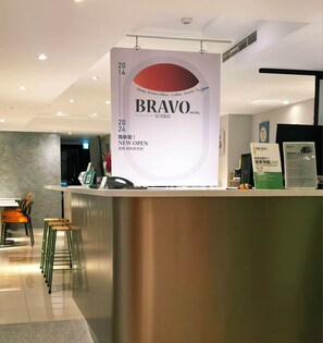A hotel reception desk with a large sign announcing a new opening. - Bravo Hotel (Taichung)