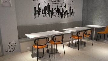 A modern cafe interior with a cityscape wall art, white tables, and orange chairs.