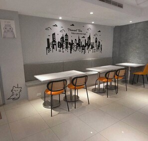 A modern cafe interior with a cityscape wall art, white tables, and orange chairs. - Bravo Hotel (Taichung)