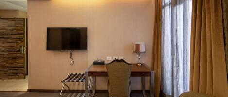 Habitación de hotel con escritorio, silla, televisor, lámpara y cortinas.