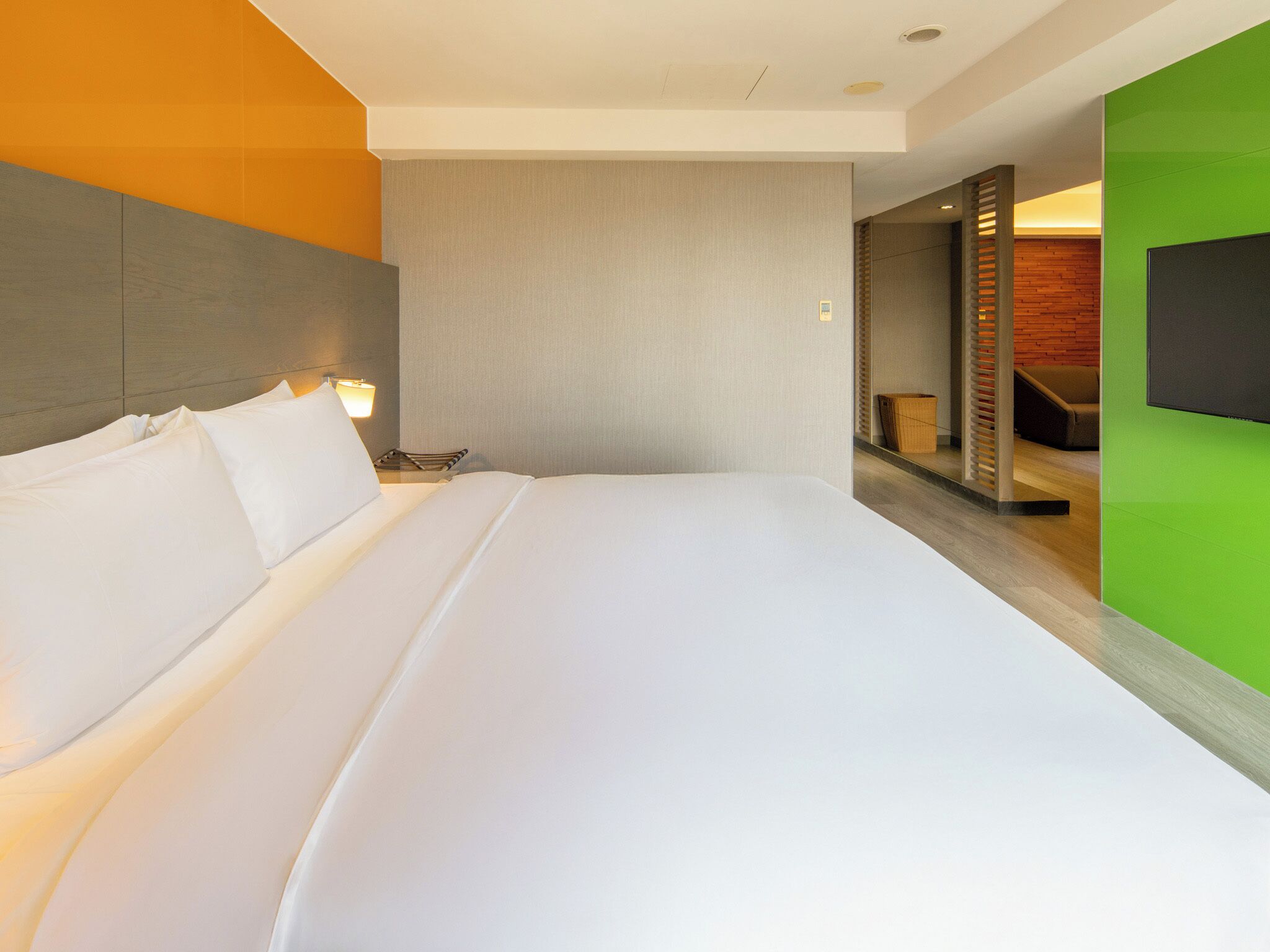 A modern hotel room with a large bed, a nightstand, a wall-mounted TV, and a wooden accent wall.