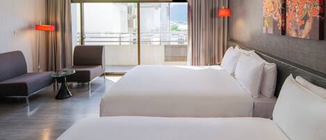 Una habitación de hotel con una cama grande, un sofá, una mesita y vistas a la ciudad a través de amplias ventanas.