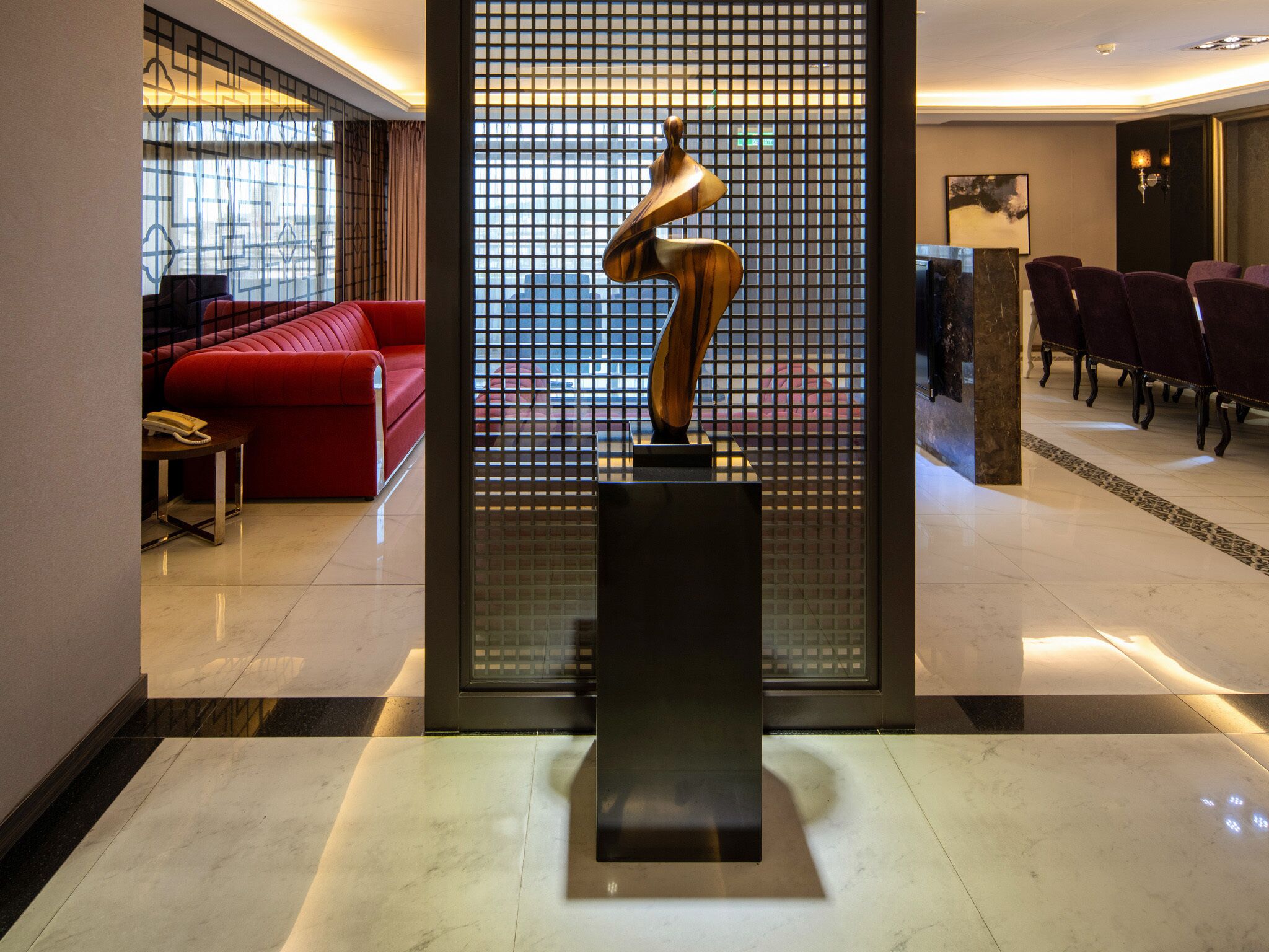 A lobby with a red sofa, a black sculpture, and a seating area with purple chairs.
