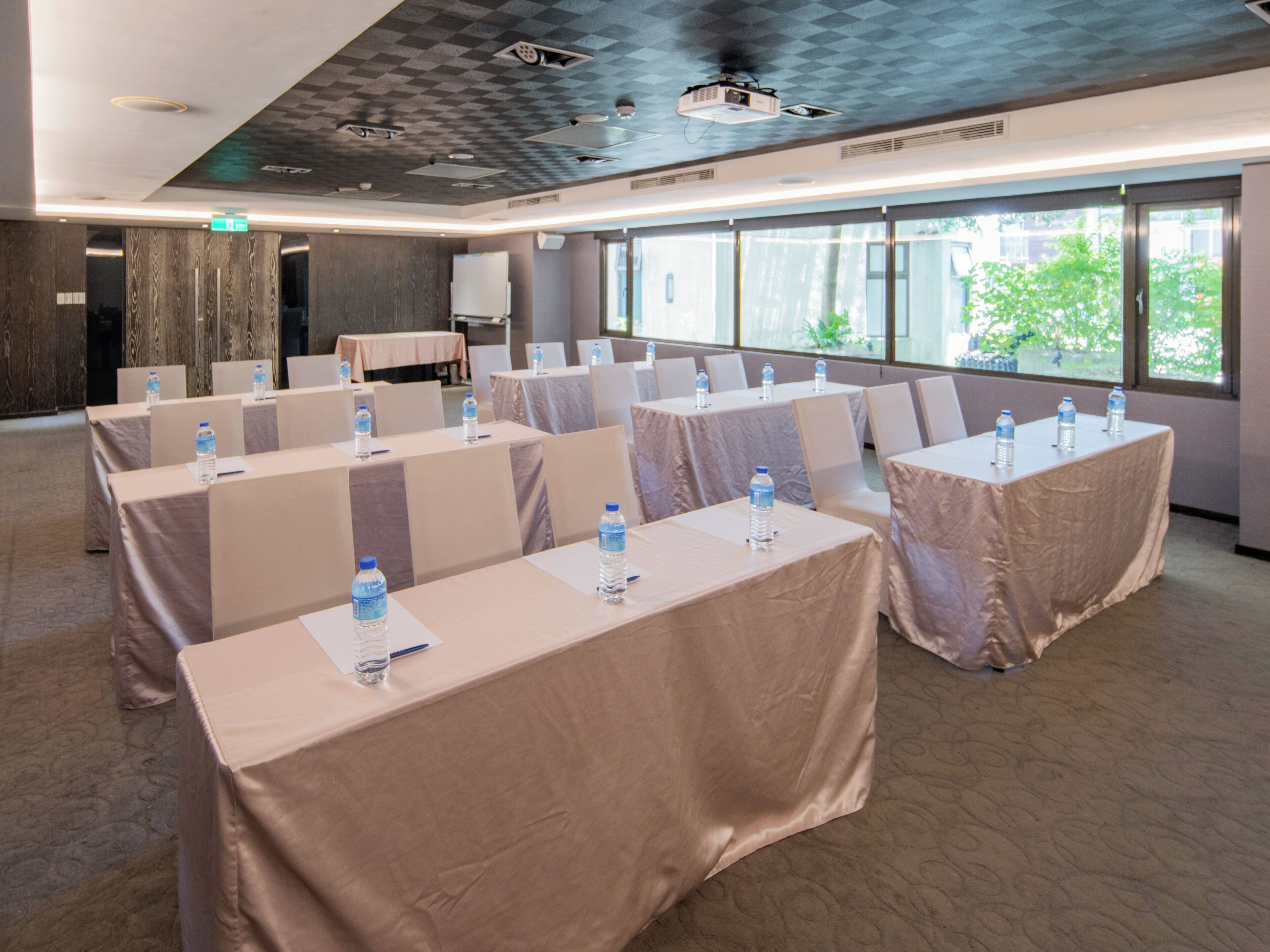 A conference room with tables set up for a meeting, equipped with water bottles, and large windows providing a view of the outdoors.