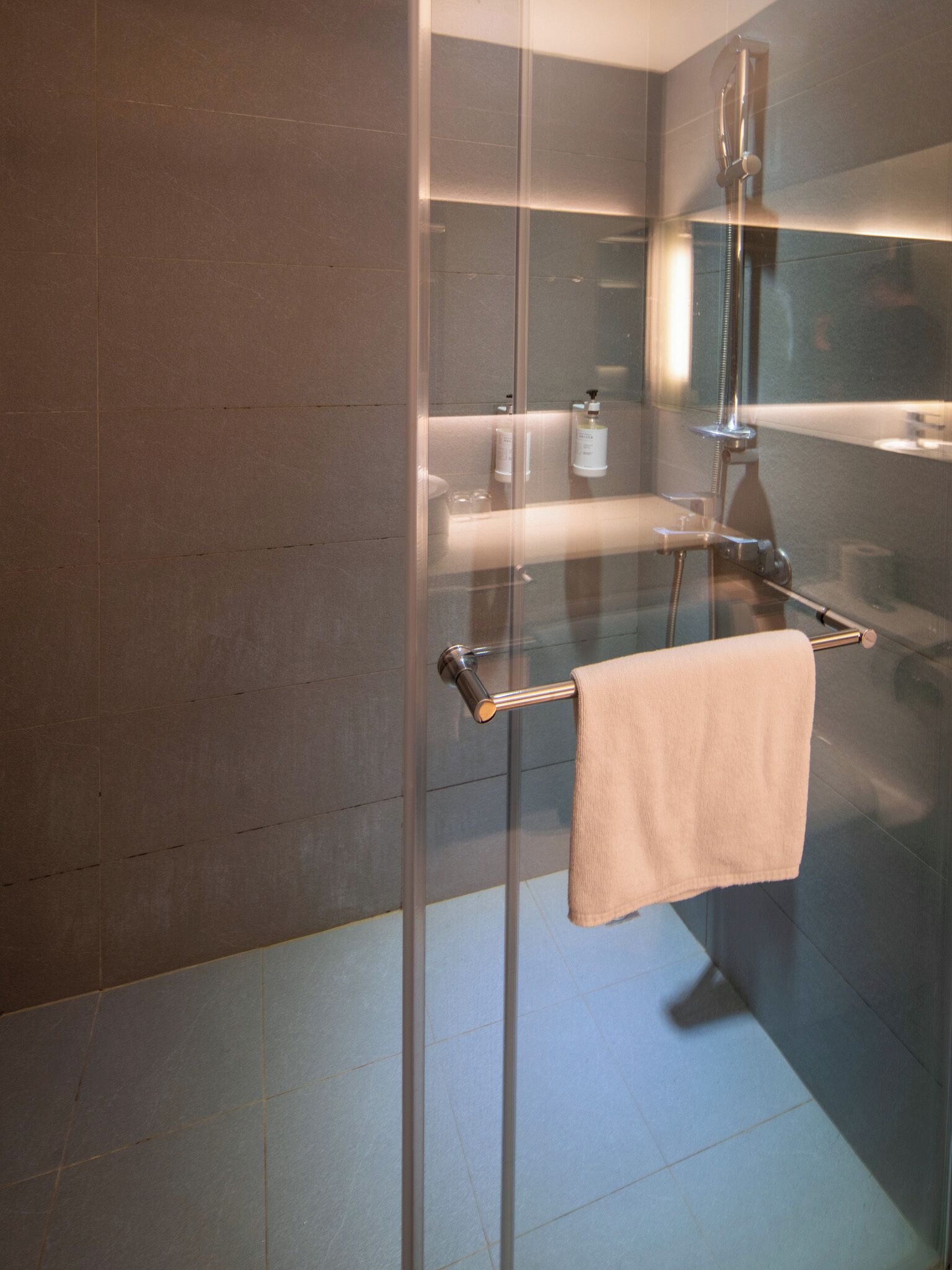 A modern bathroom with a glass shower enclosure, a towel rack, and a mirror.