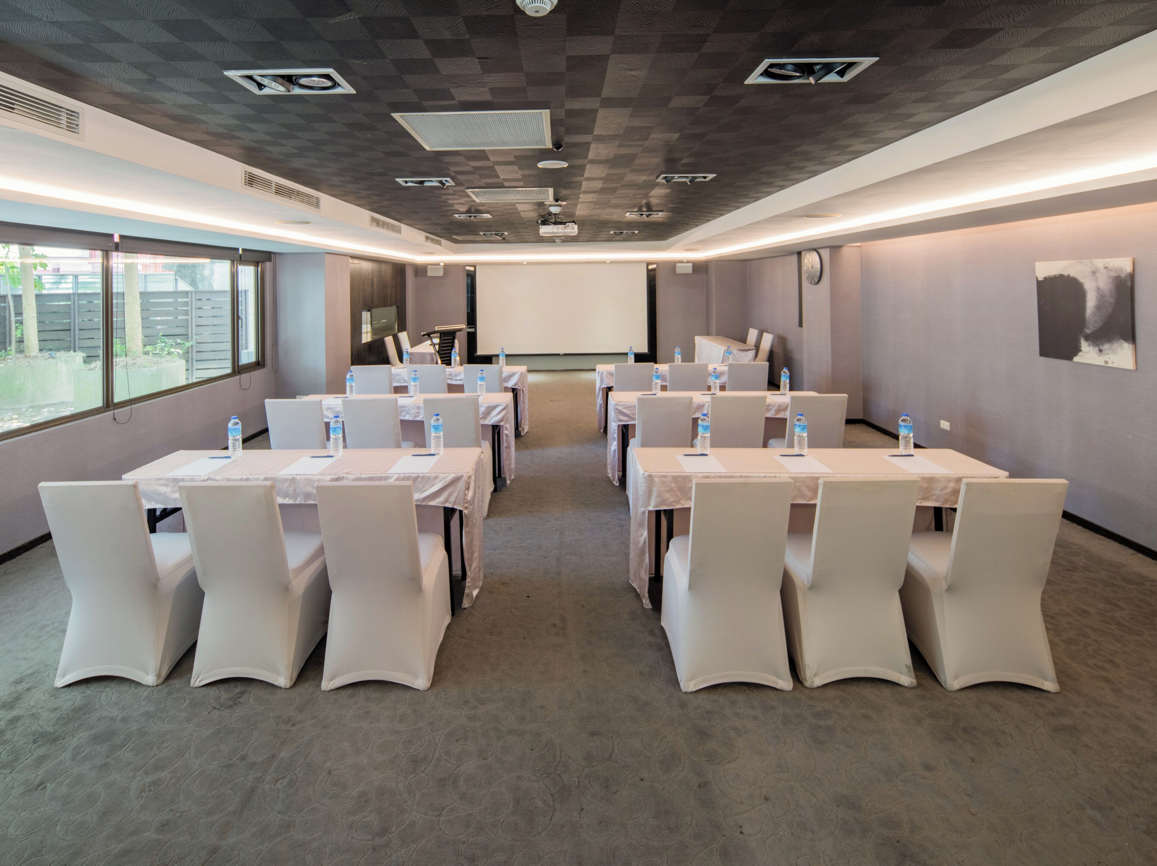 A conference room with tables and chairs, a projector screen, and a large window.
