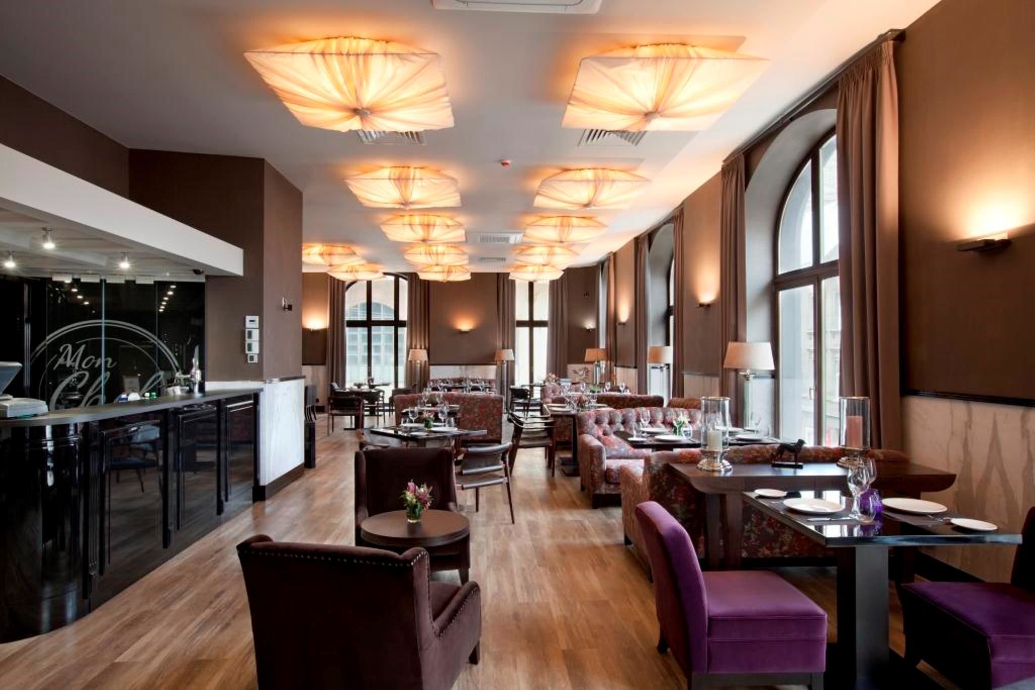 Un amplio vestíbulo de hotel con zona de bar, varios arreglos de asientos y ventanas grandes que dejan entrar luz natural.