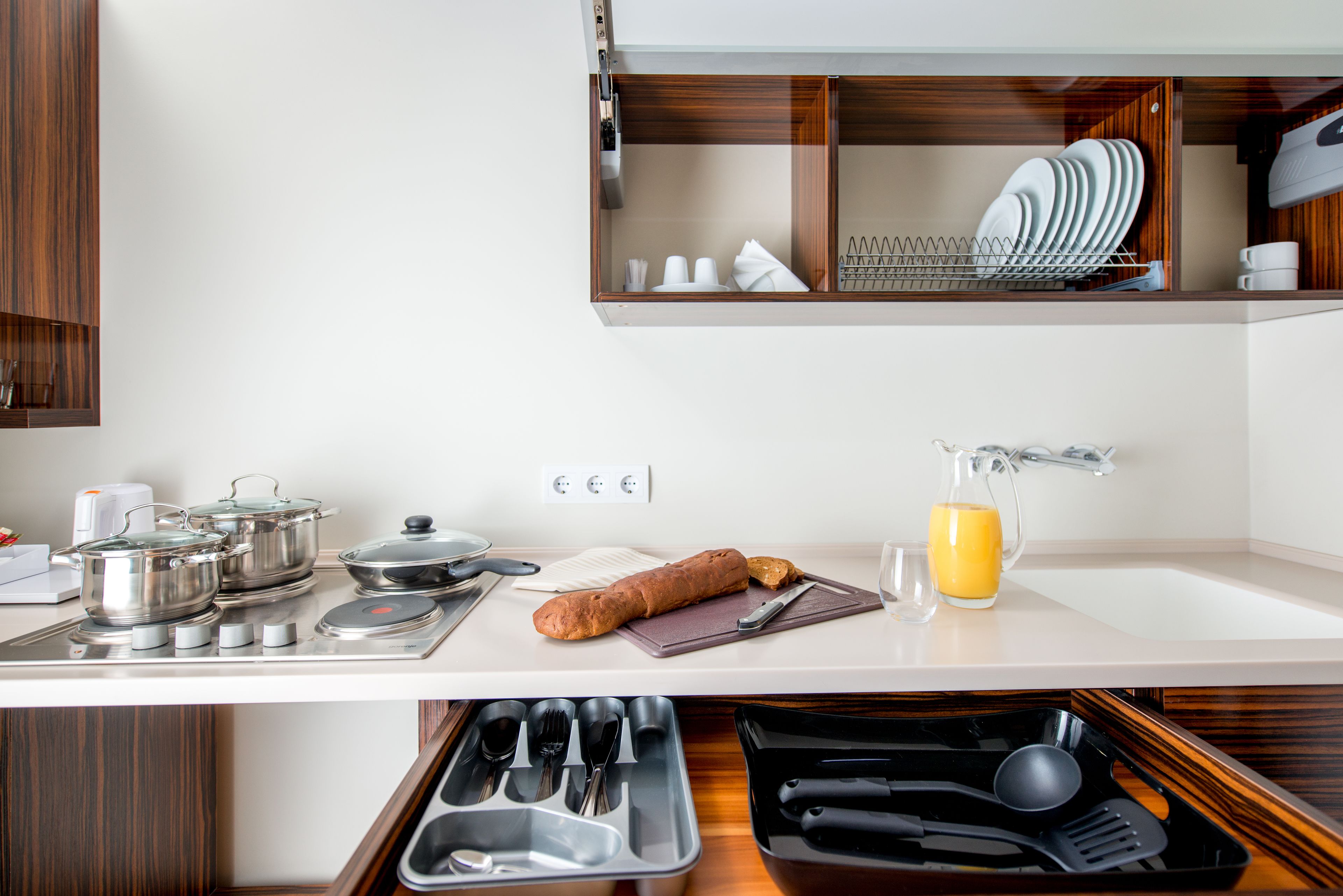 A modern kitchen with stainless steel appliances, a bread loaf, a juice pitcher, and neatly organized utensils.