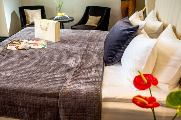Una cama bien hecha con un edredón marrón, una revista y un bolso blanco encima.