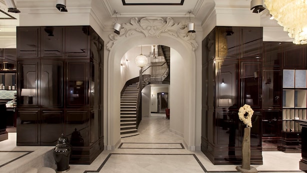 A grand hallway with a marble floor, a central staircase, and dark wooden paneling on the walls.