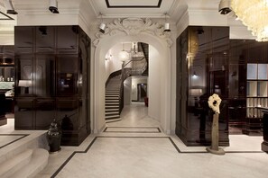 Un amplio pasillo con piso de mármol, una escalera central y paneles de madera oscura en las paredes.