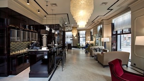 A spacious hotel lobby with a grand chandelier, a bar area, and a seating area with a red chair.