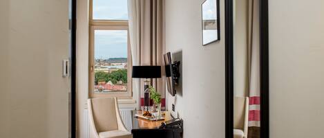 Habitación de hotel con un gran ventanal arqueado, un escritorio con lámpara, una silla y vistas a la ciudad.