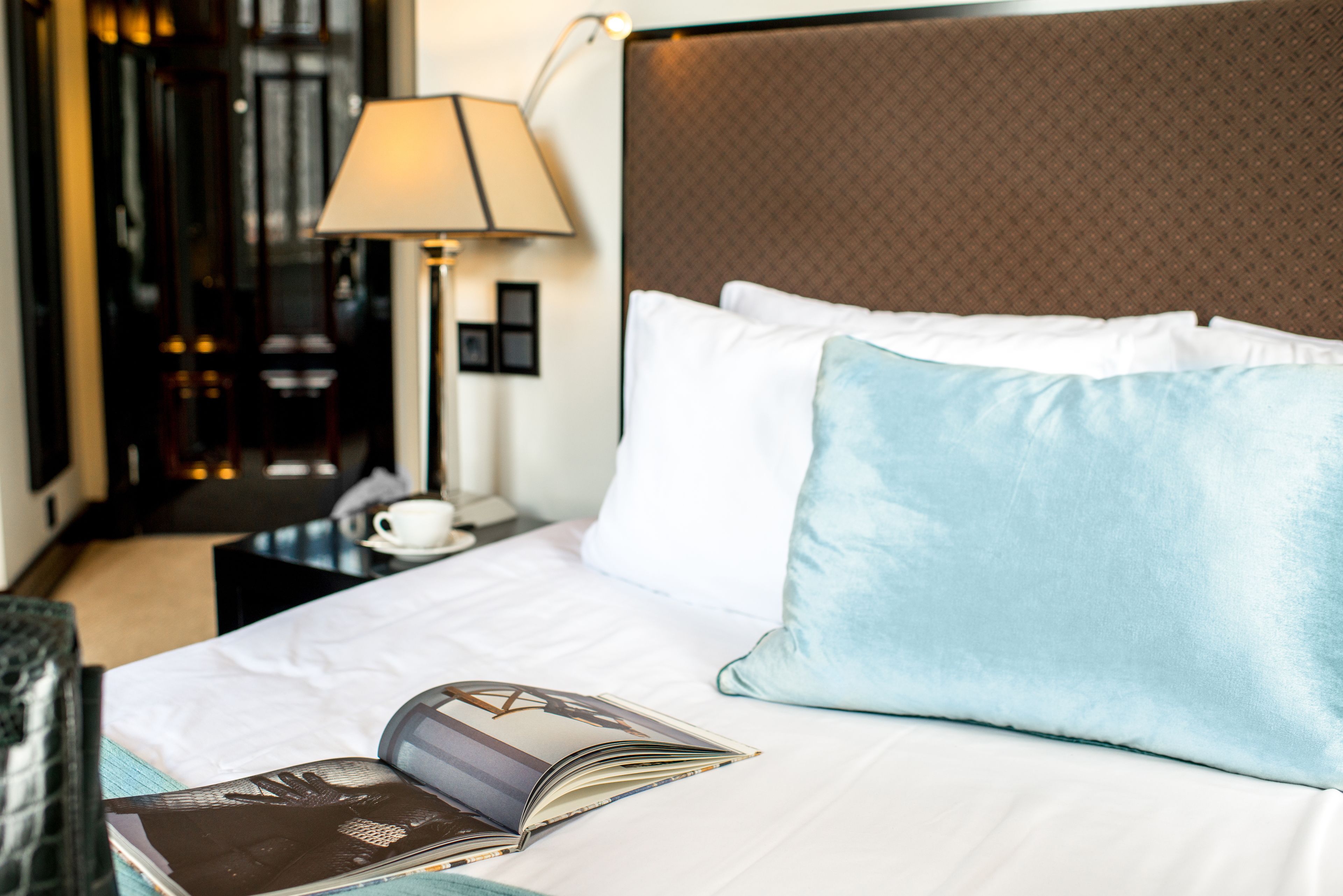 A neatly made bed with a book, pillows, and a lamp.