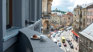 A balcony with a cup and pastry, overlooking a busy street with historic buildings.