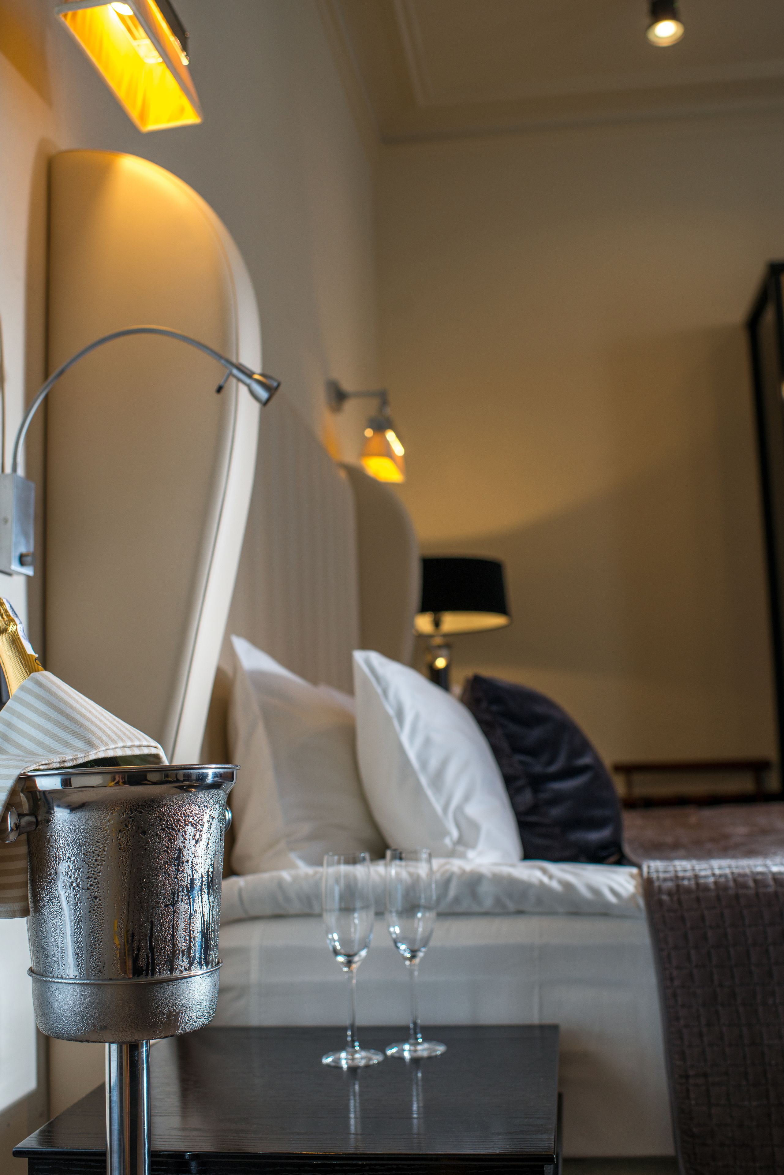 Quarto de hotel com cama, mesa de cabeceira e luminárias.