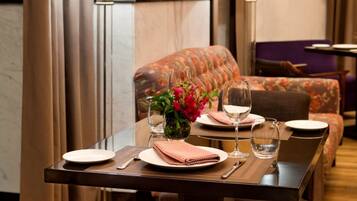 A dining area with a table set for two, featuring a vase of flowers, wine glasses, and neatly arranged plates and cutlery.