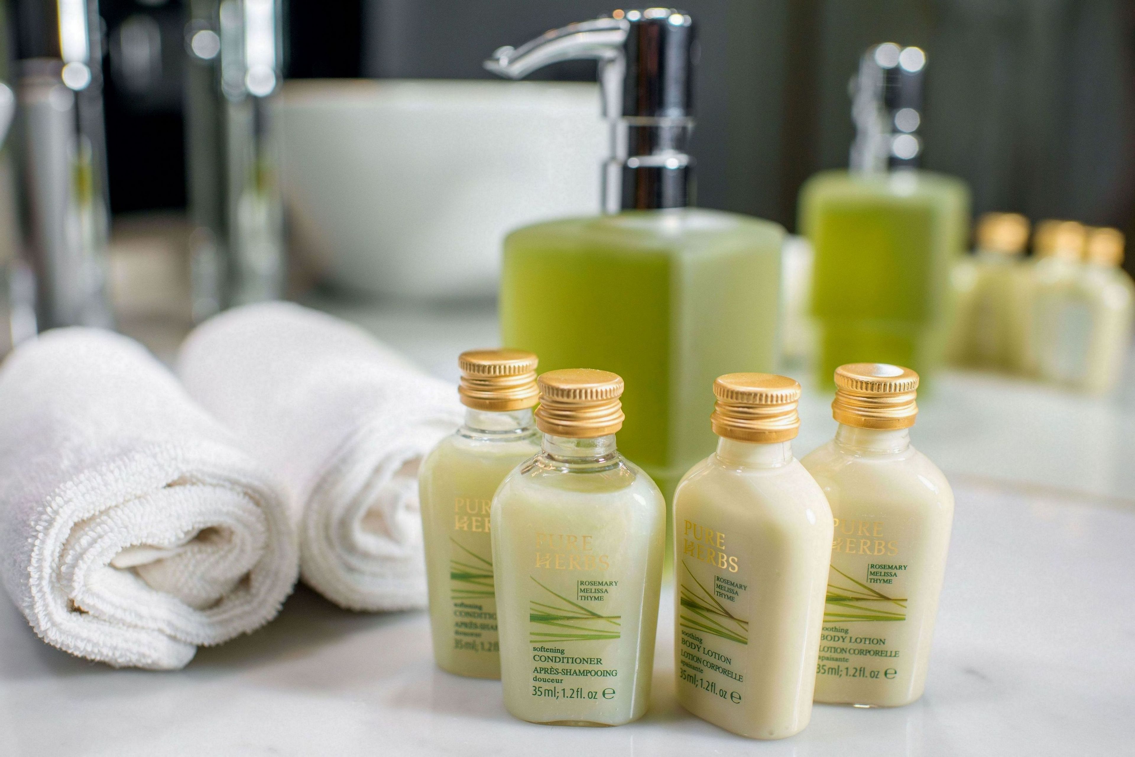 A bathroom with a large mirror, a green soap dispenser, and several bottles of body lotion.