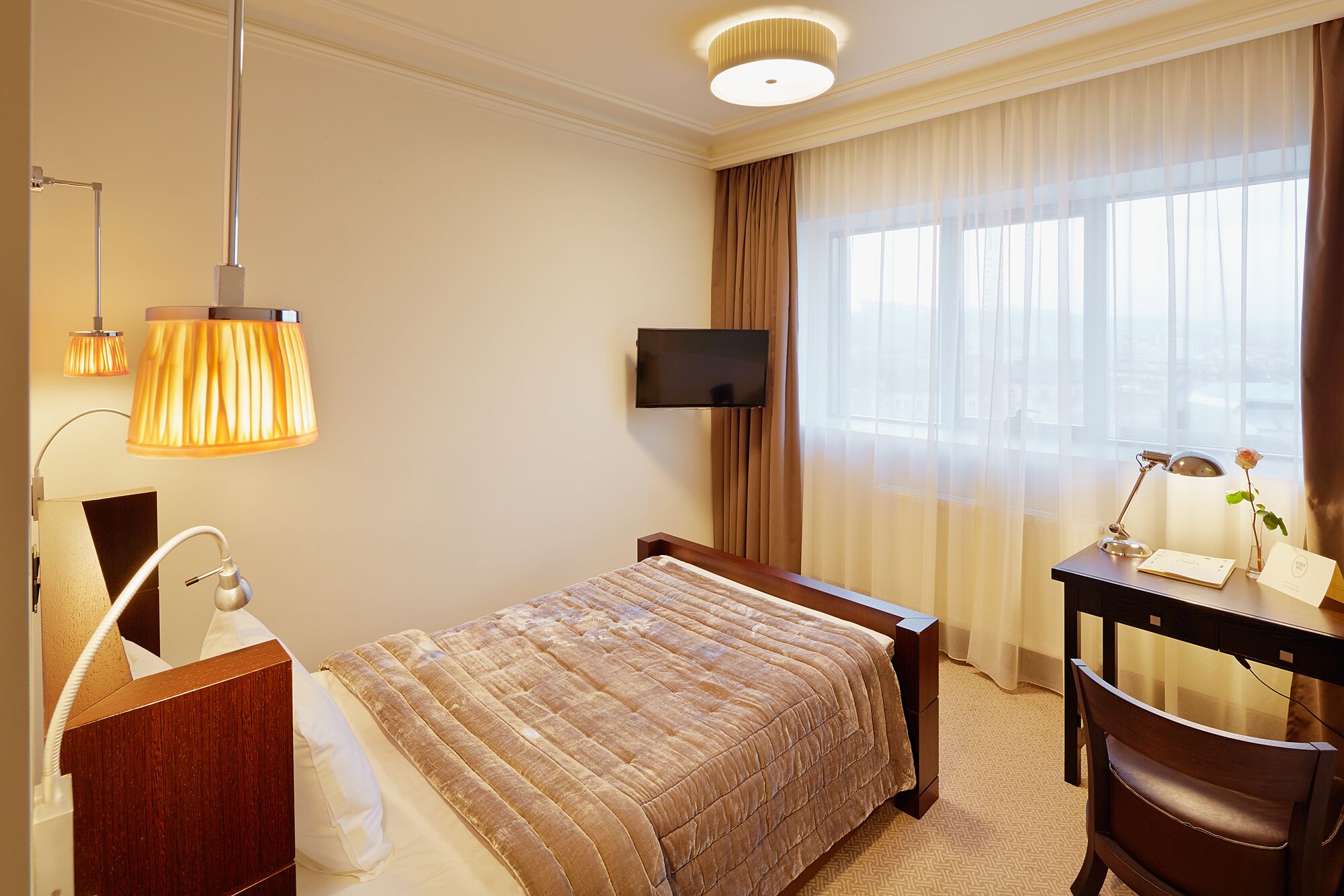 A hotel room with a bed, a desk, a television, and a window with curtains.