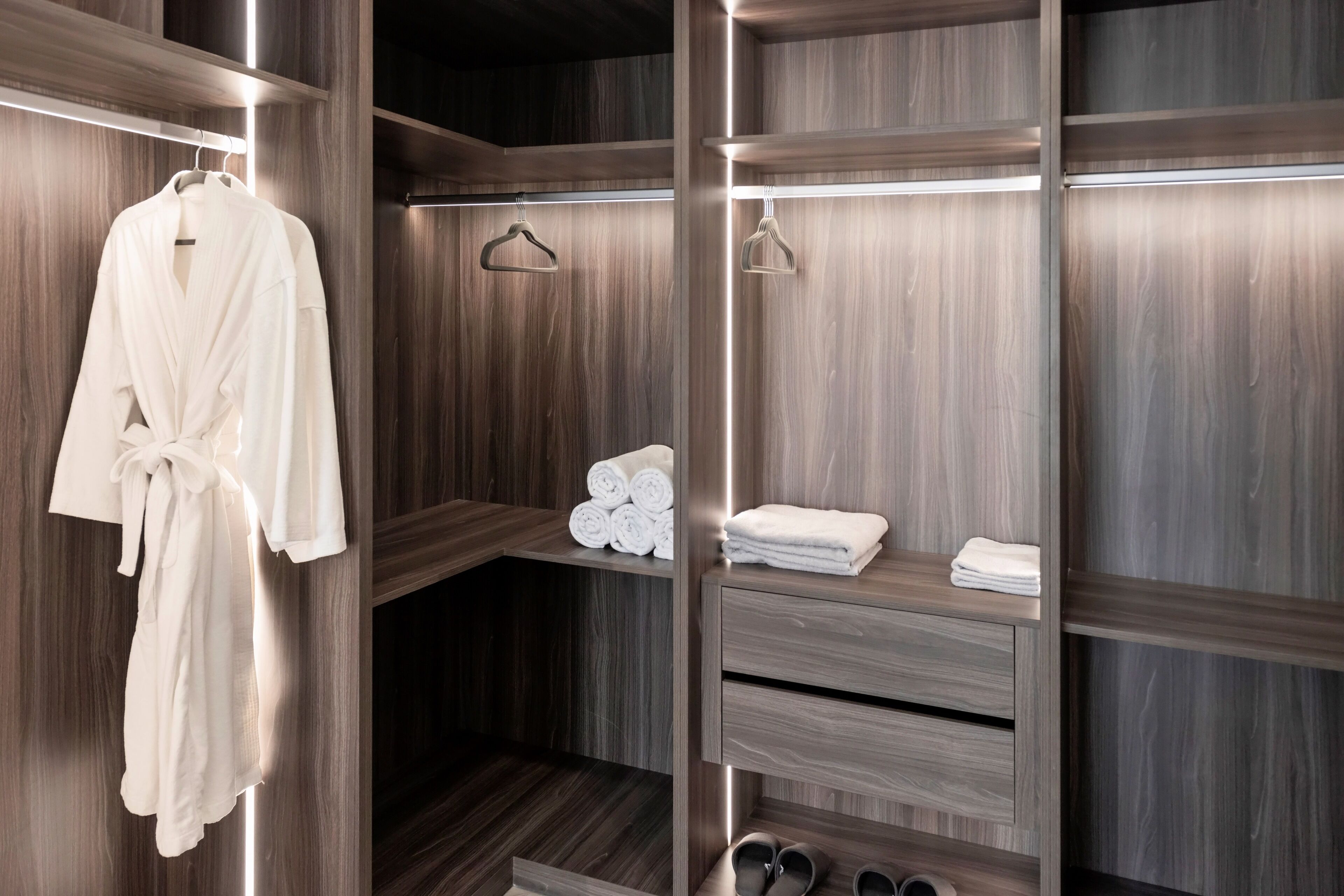 A walk-in closet with wooden shelving, a hanging robe, and neatly folded towels.