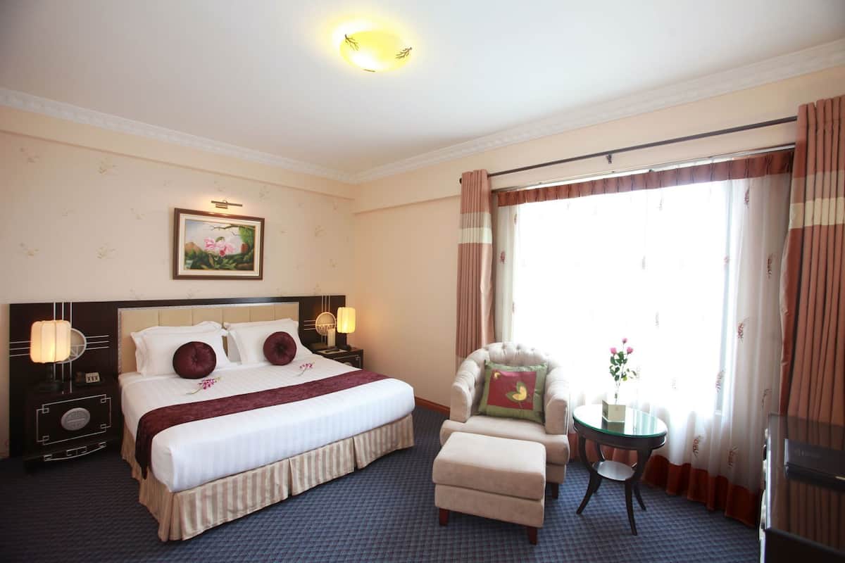 A hotel room with a large bed, a chair, a small table, and a window with curtains.