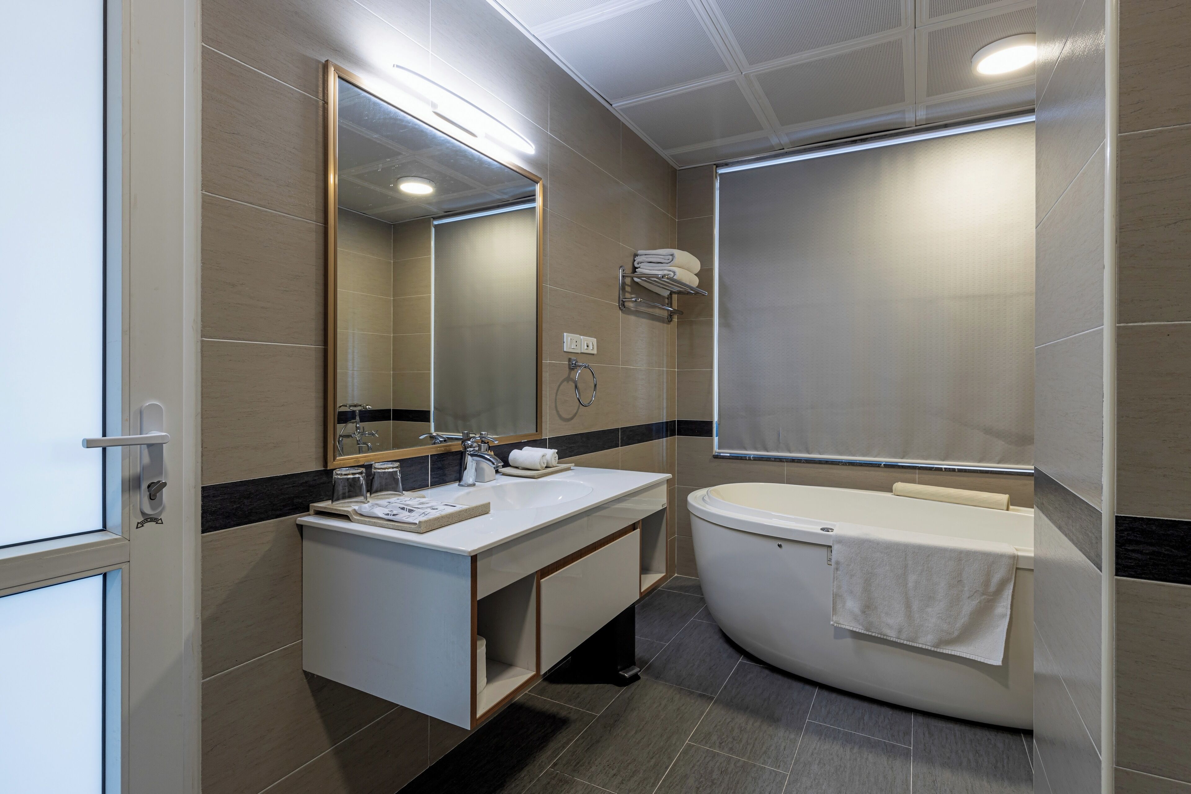 A modern bathroom with a white vanity, a large mirror, a bathtub, and a towel rack.