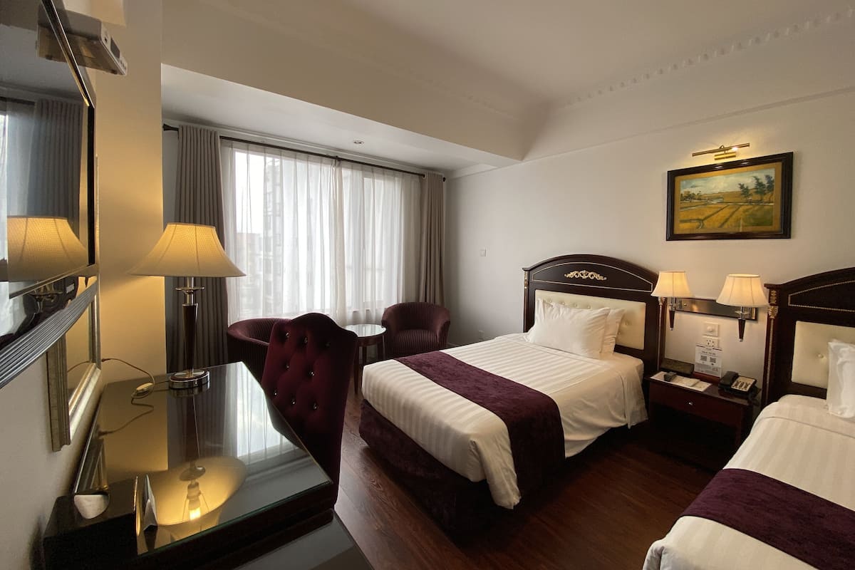 A hotel room with two beds, a desk, a chair, and a painting on the wall.
