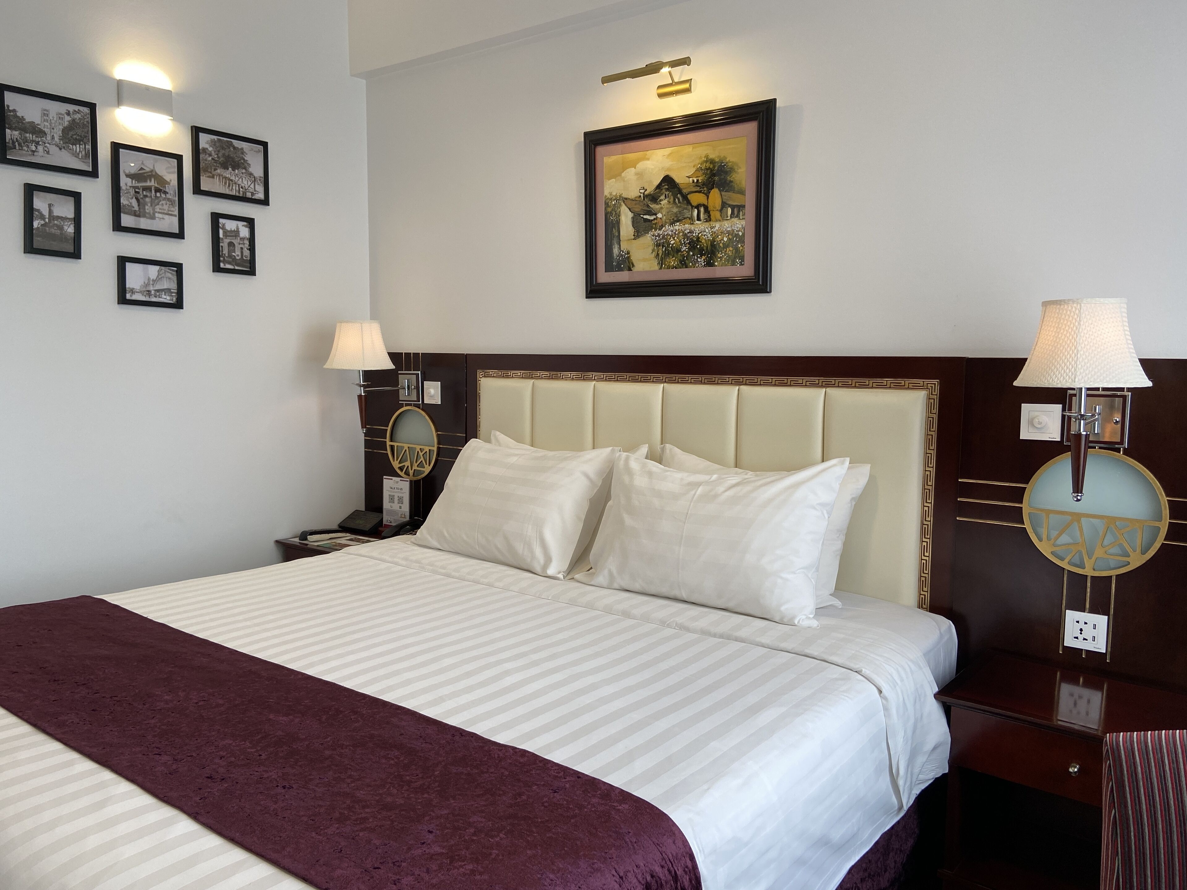 Une chambre d’hôtel avec un grand lit, deux lampes de chevet, une table de chevet, un tableau encadré au mur et un applique décorative.