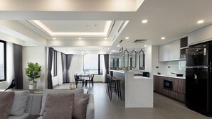 A modern kitchen with a built-in LG refrigerator, a dining area with a white marble island, and a view of the city through large windows. - Flower Garden Hotel (Hanoi)