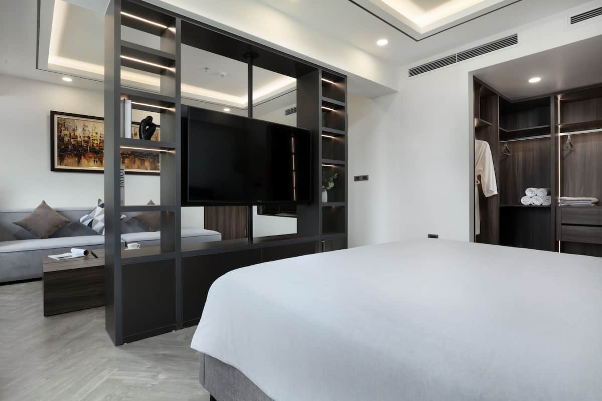 A modern bedroom with a large bed, a TV, a sofa, and a walk-in closet.