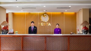 A reception desk with a logo, two staff members, and decorative lamps. -  Nesta Hotel Ha Noi (Hanoi)