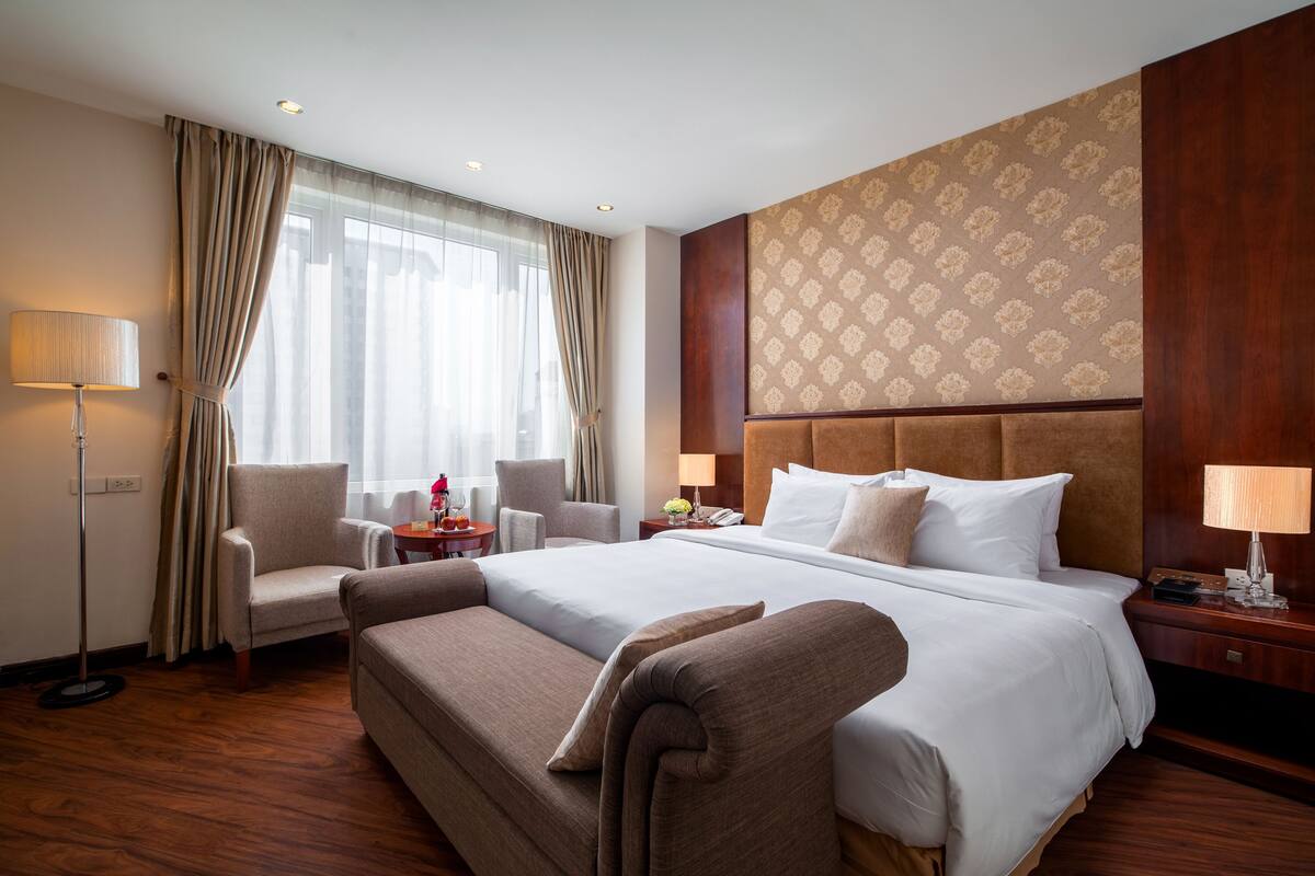 A hotel room with a large bed, two armchairs, a desk, and a lamp.