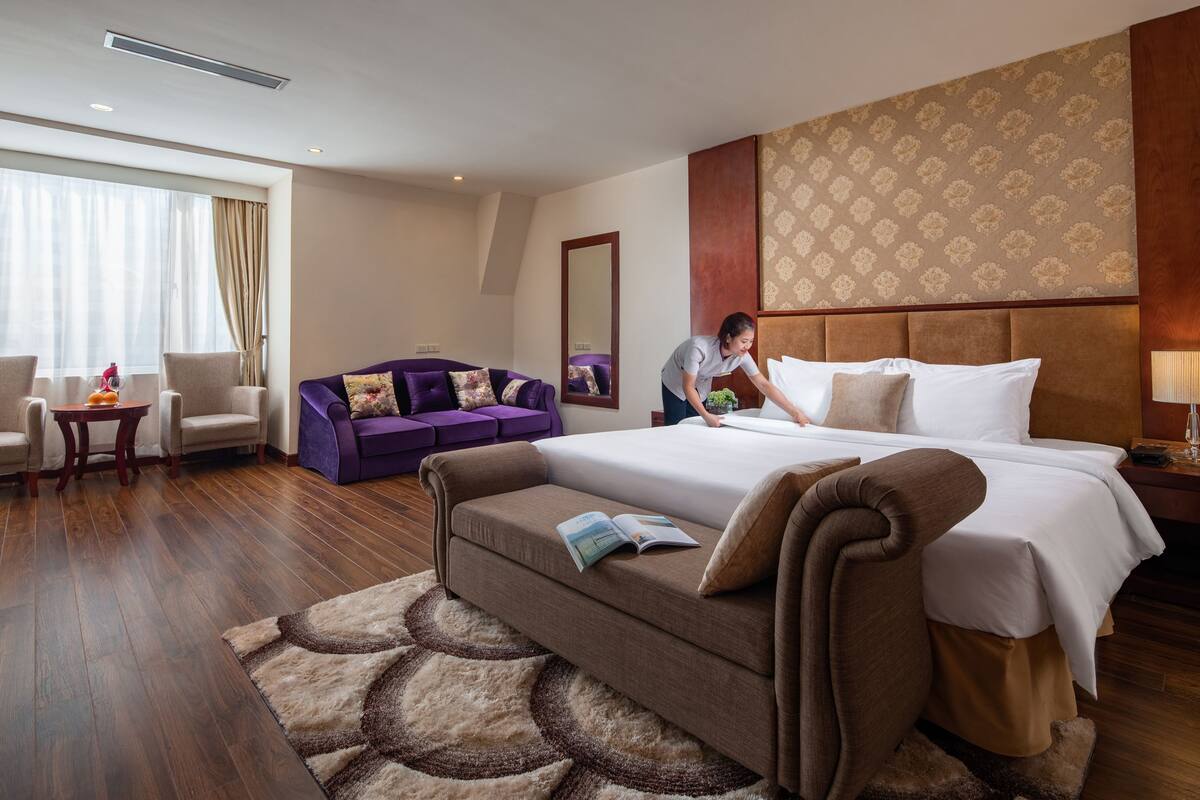 A hotel room with a large bed, a sofa, a chair, and a small table.