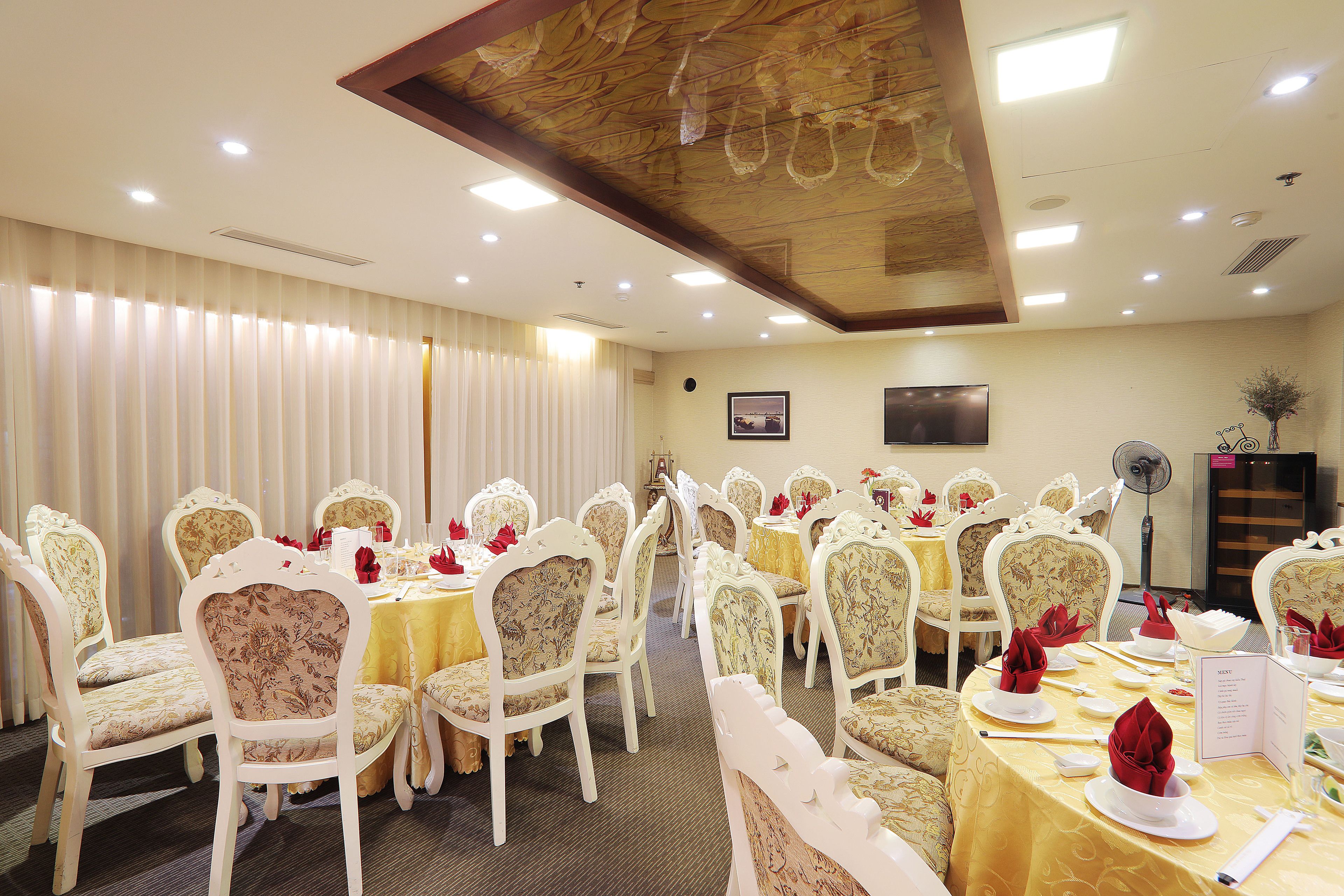 A banquet hall with round tables, white upholstered chairs, and a ceiling with recessed lighting.