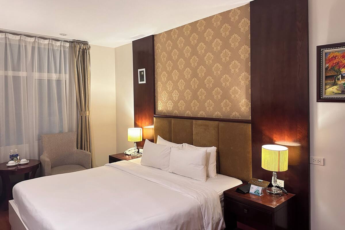 A hotel room with a large bed, two bedside tables with lamps, a chair, and a painting on the wall.