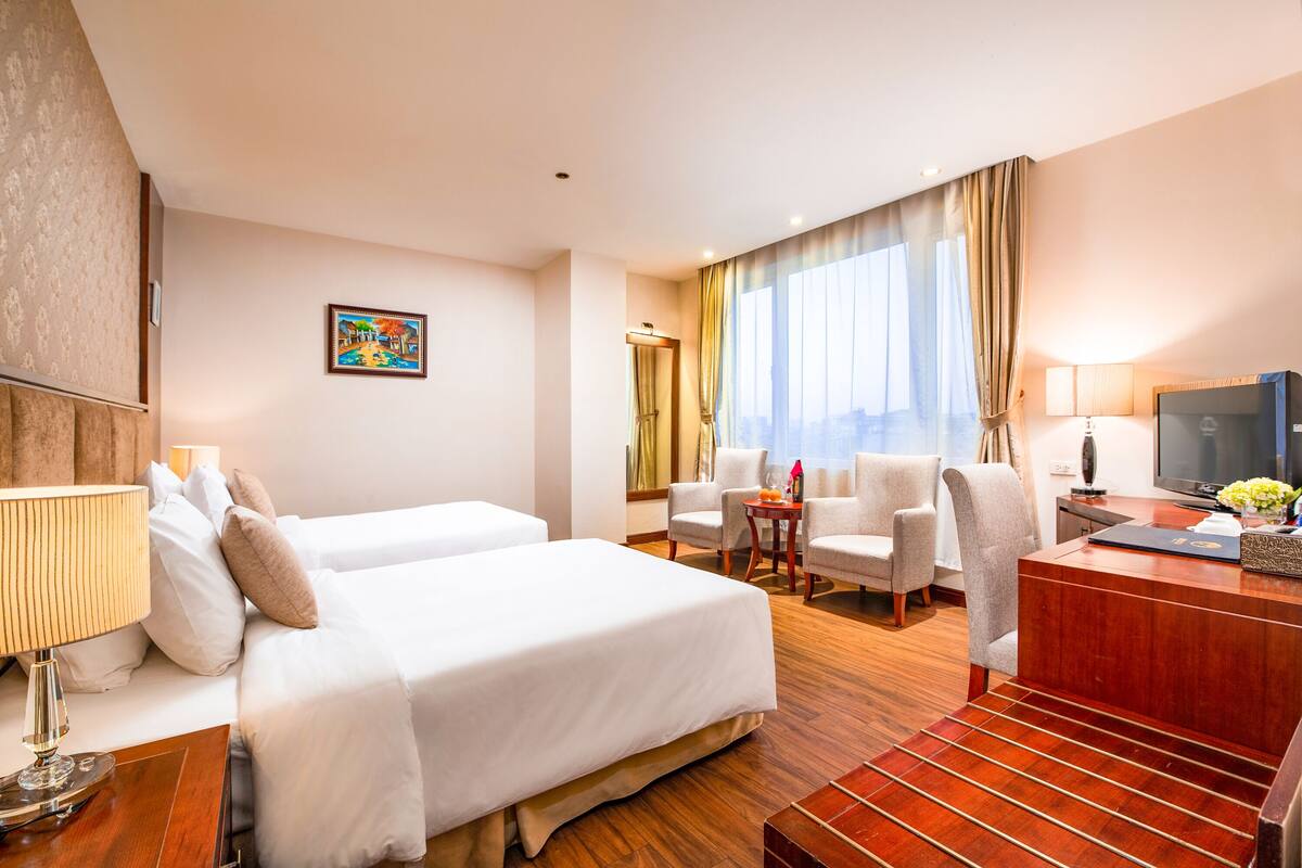 A hotel room with two beds, a desk with a television, a chair, and a window with curtains.