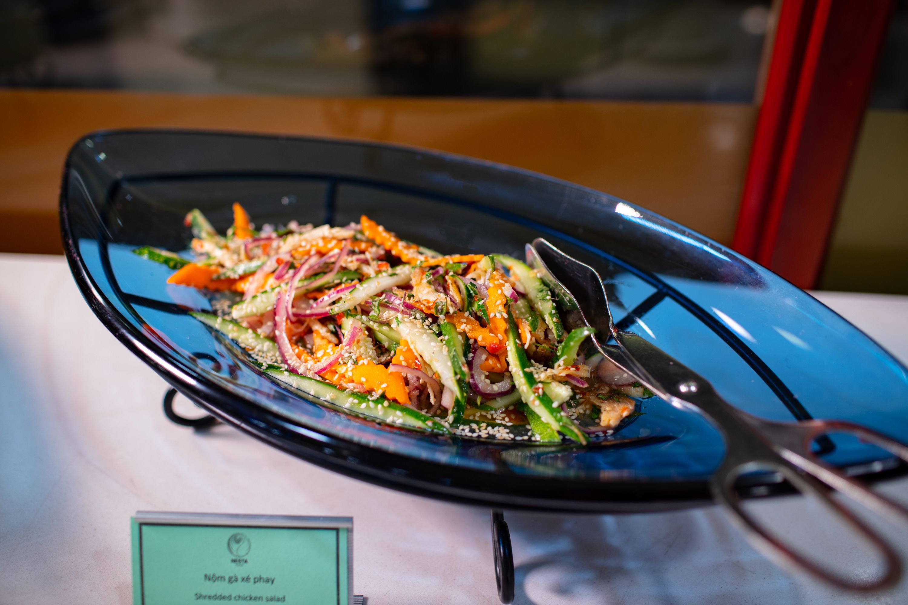A blue glass plate with a shredded chicken salad, accompanied by a pair of scissors.