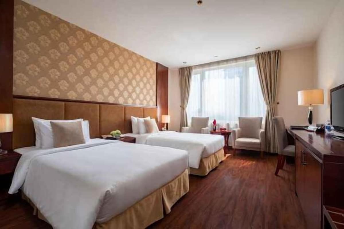 A hotel room with two beds, a desk, a chair, a TV, and a window with curtains.