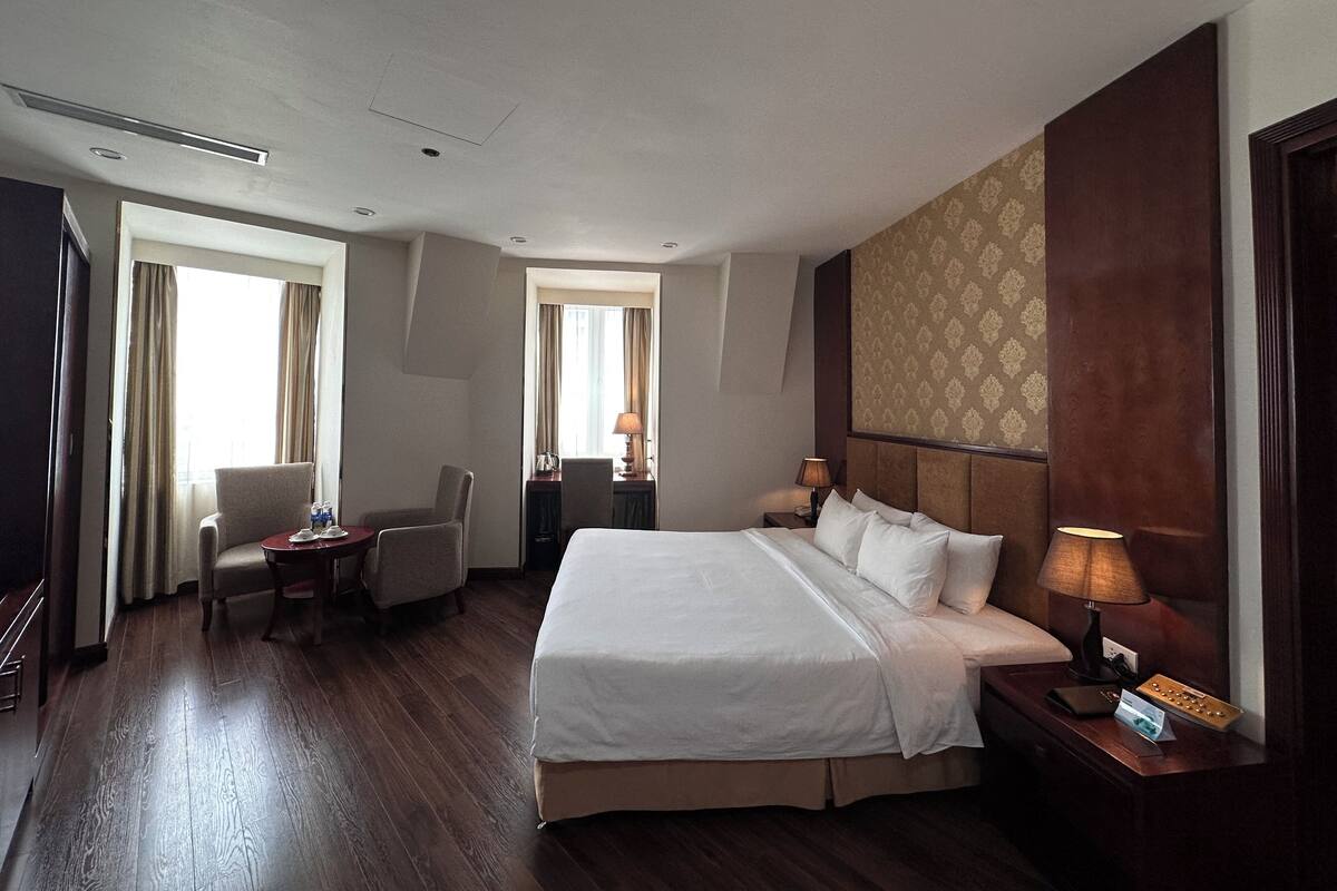 A hotel room with a large bed, two armchairs, a desk, and a window with curtains.