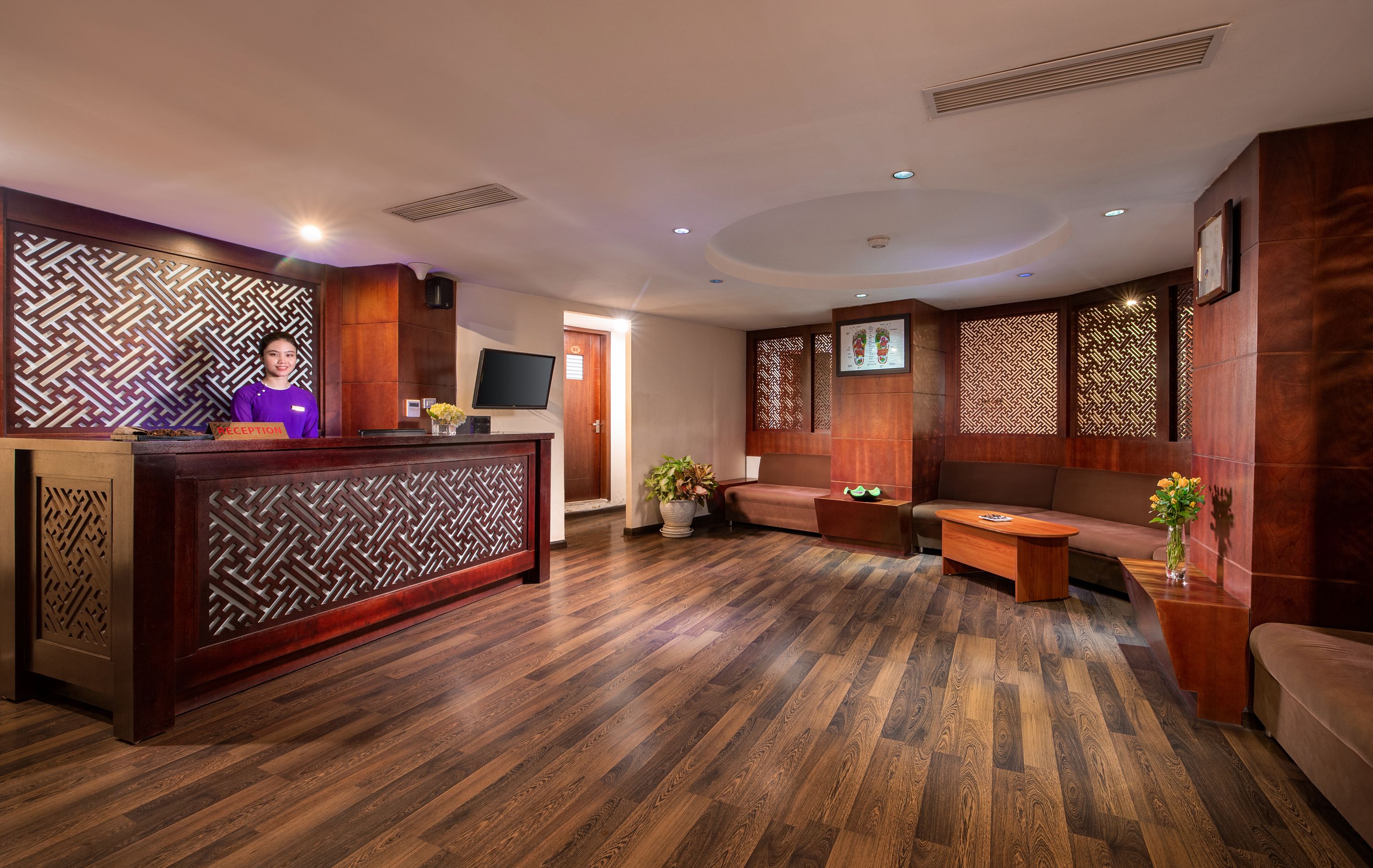 A reception area with a wooden reception desk, a sofa, and a television on the wall.