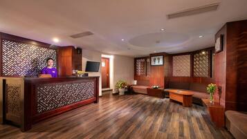 A reception area with a wooden reception desk, a sofa, and a television on the wall.