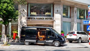 A black van parked in front of the NESTA HANOI HOTEL with a visible rear seat and a logo on the side. -  Nesta Hotel Ha Noi (Hanoi)