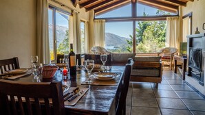 A dining area with a table set for two, a fireplace, and a view of the mountains. - Estancia del Carmen (San Carlos de Bariloche)